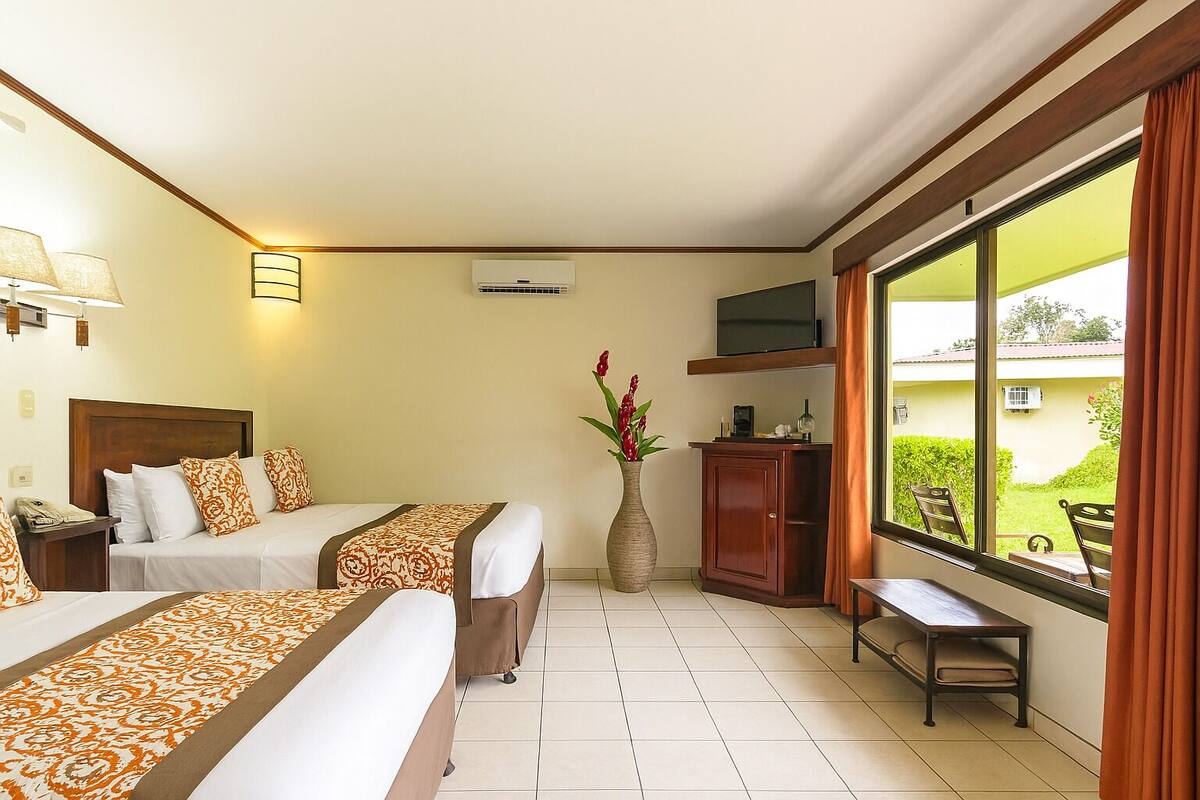 A hotel room with two beds, a TV, a desk, and a window with a view of the outdoors.