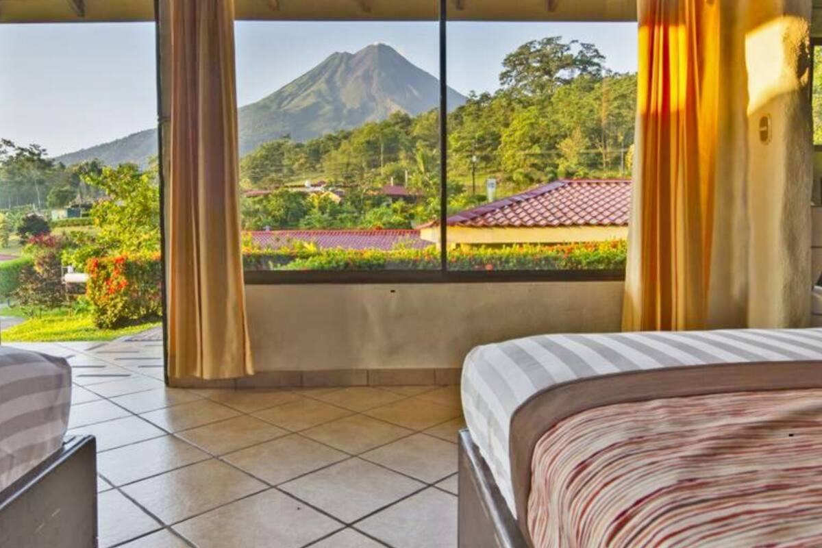 A hotel room with two beds, a large window with a view of a mountain and lush greenery.