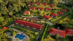 An aerial view of a resort with multiple buildings, a swimming pool, and well-maintained gardens.