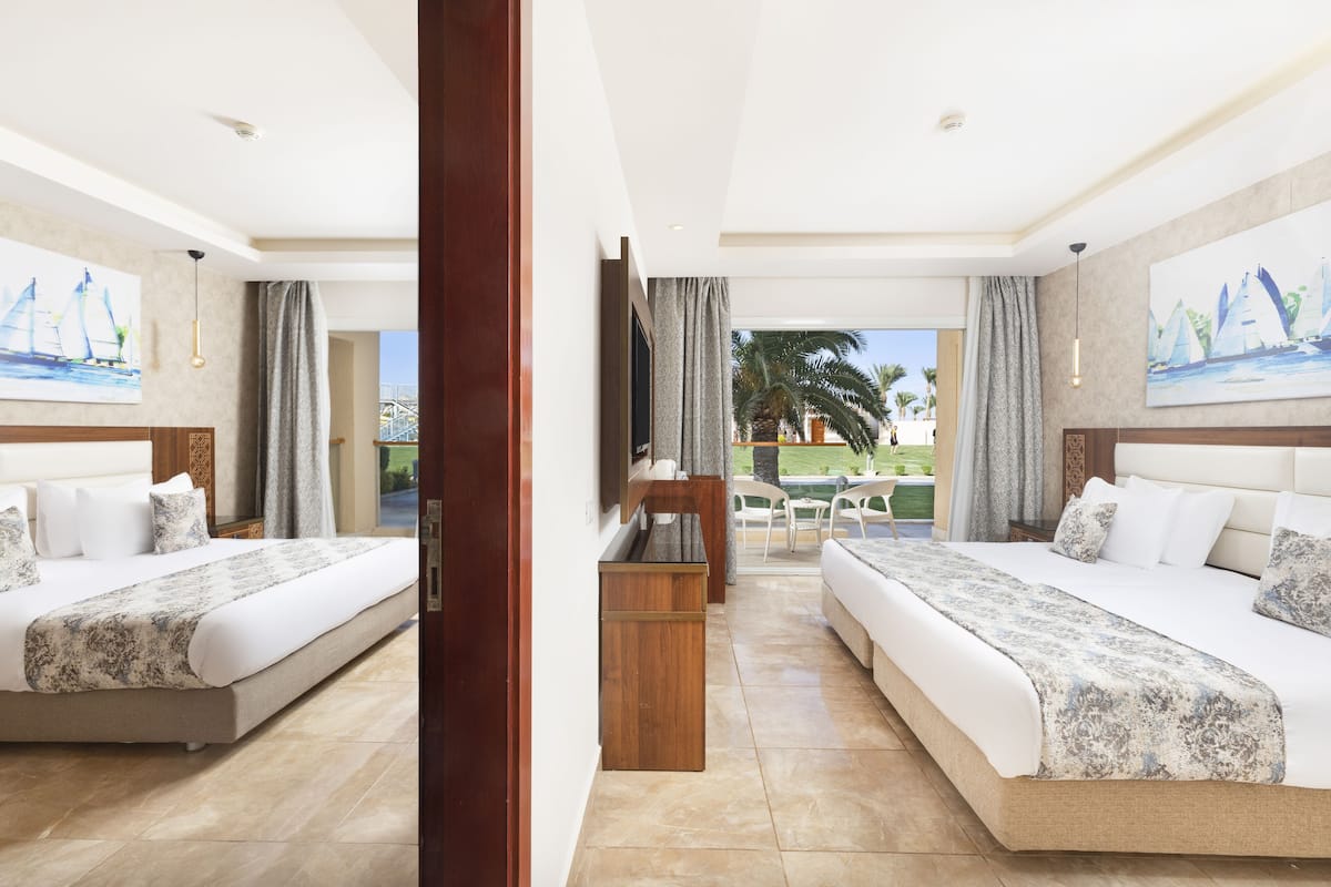 A hotel room with two beds, a wooden nightstand, a TV, and a view of a pool and palm trees.