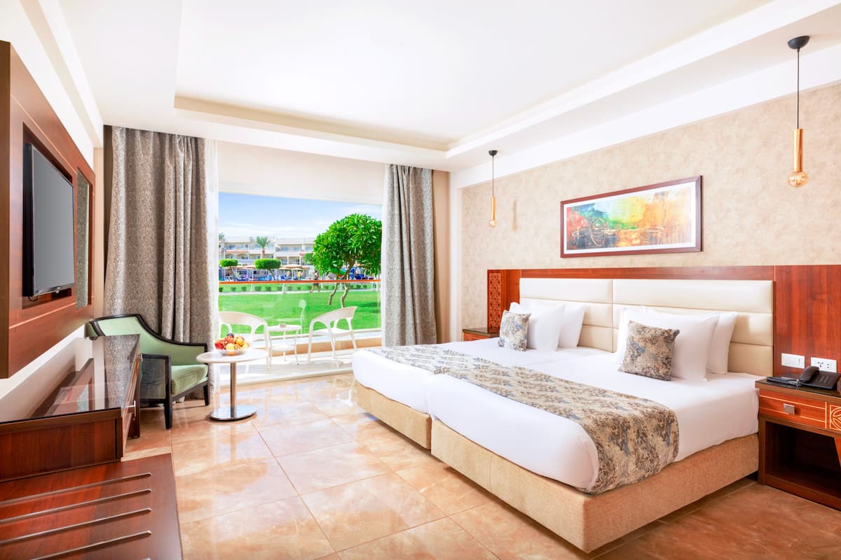 A hotel room with a large bed, a desk, a chair, and a window with a view of a green landscape.