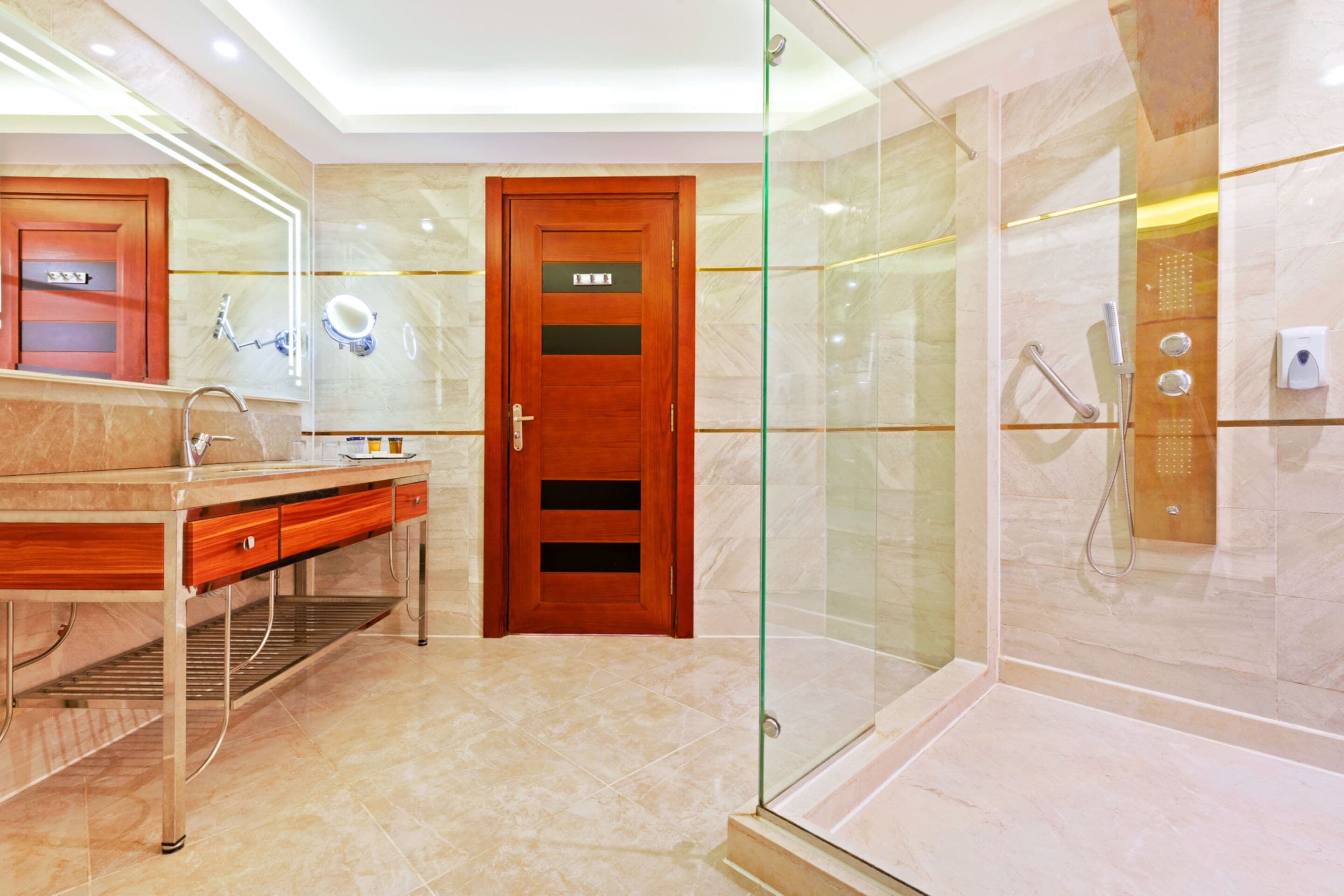 A modern bathroom with a glass-enclosed shower, a wooden door, and a vanity with a mirror.