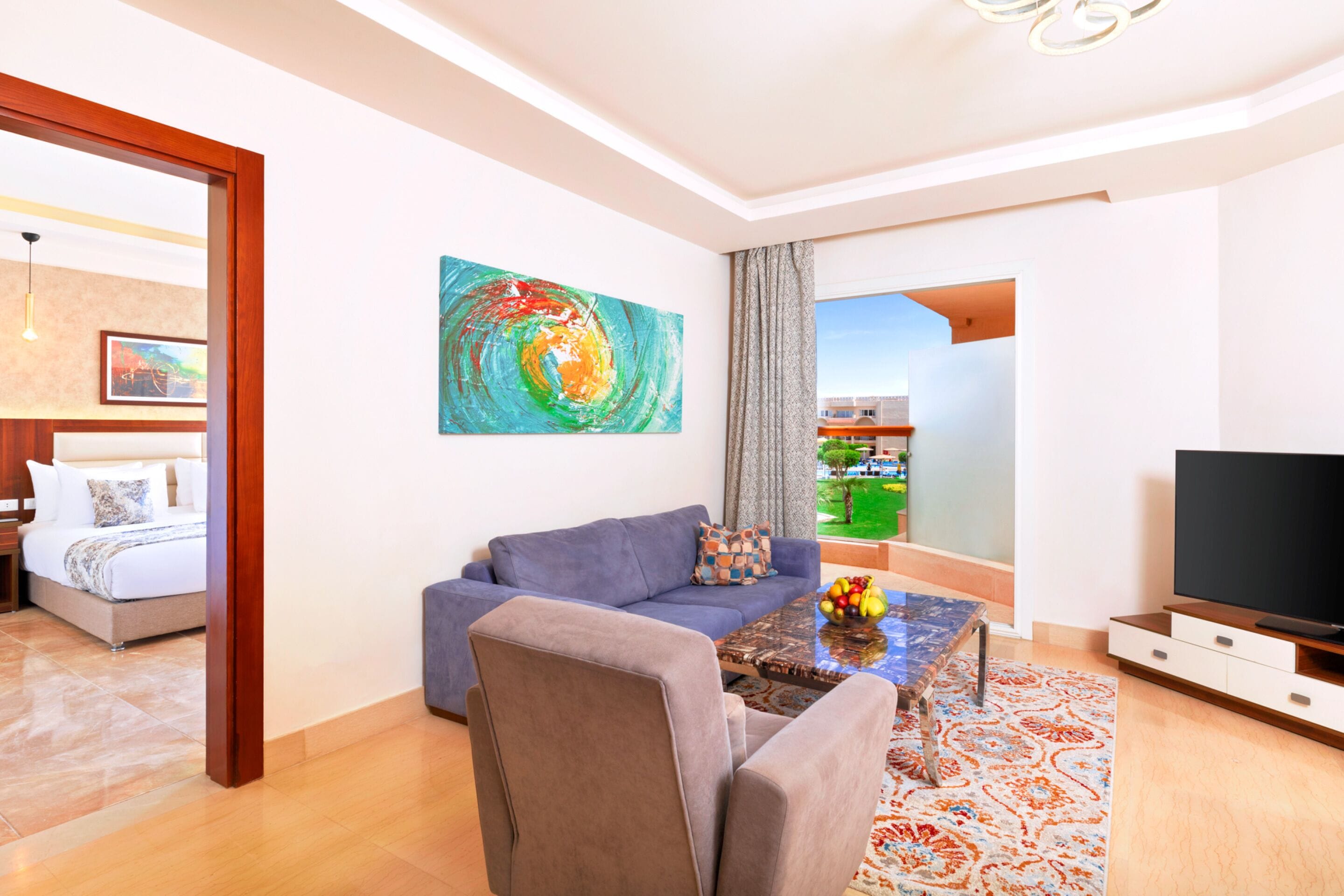 A modern living room with a sofa, coffee table, and TV. A painting is on the wall, and there's a view of the outdoors through a window.