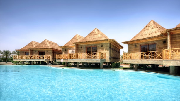 A resort with multiple overwater bungalows, each with a thatched roof and wooden balcony, overlooking a clear blue pool. - Pickalbatros Aqua Blu Sharm El Sheikh (Sharm El Sheikh)