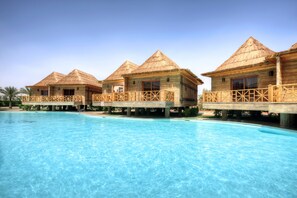Un resort con varias cabañas sobre el agua, cada una con techo de paja y balcón de madera, con vistas a una piscina azul cristalina.