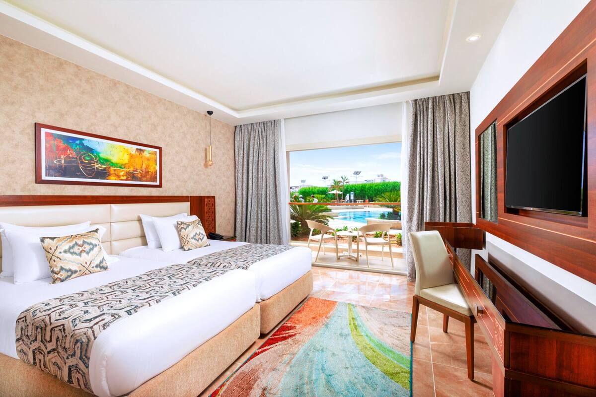 A hotel room with a bed, a TV, a desk, and a view of a pool.