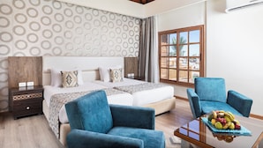 A bedroom with a large bed, two blue armchairs, a wooden nightstand, and a fruit bowl on a glass table. - Pickalbatros Aqua Blu Sharm El Sheikh (Sharm El Sheikh)