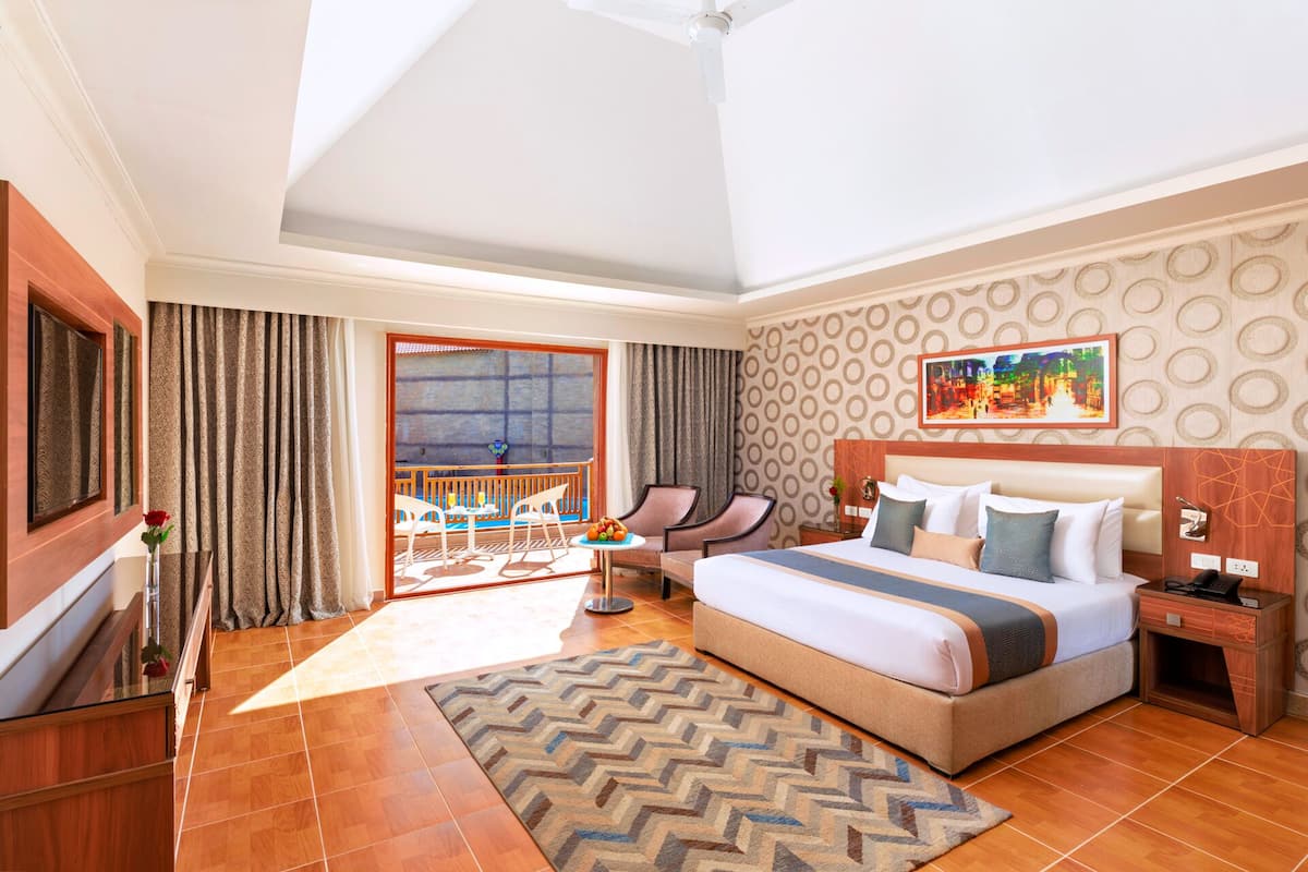 A hotel room with a large bed, a desk, a chair, a TV, and a balcony with a view.