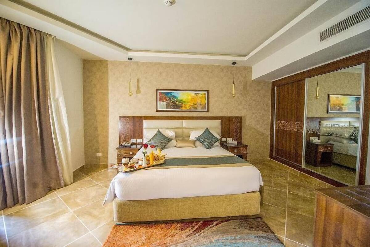 A hotel room with a large bed, a wooden headboard, a nightstand, a dresser, a mirror, and a painting on the wall.