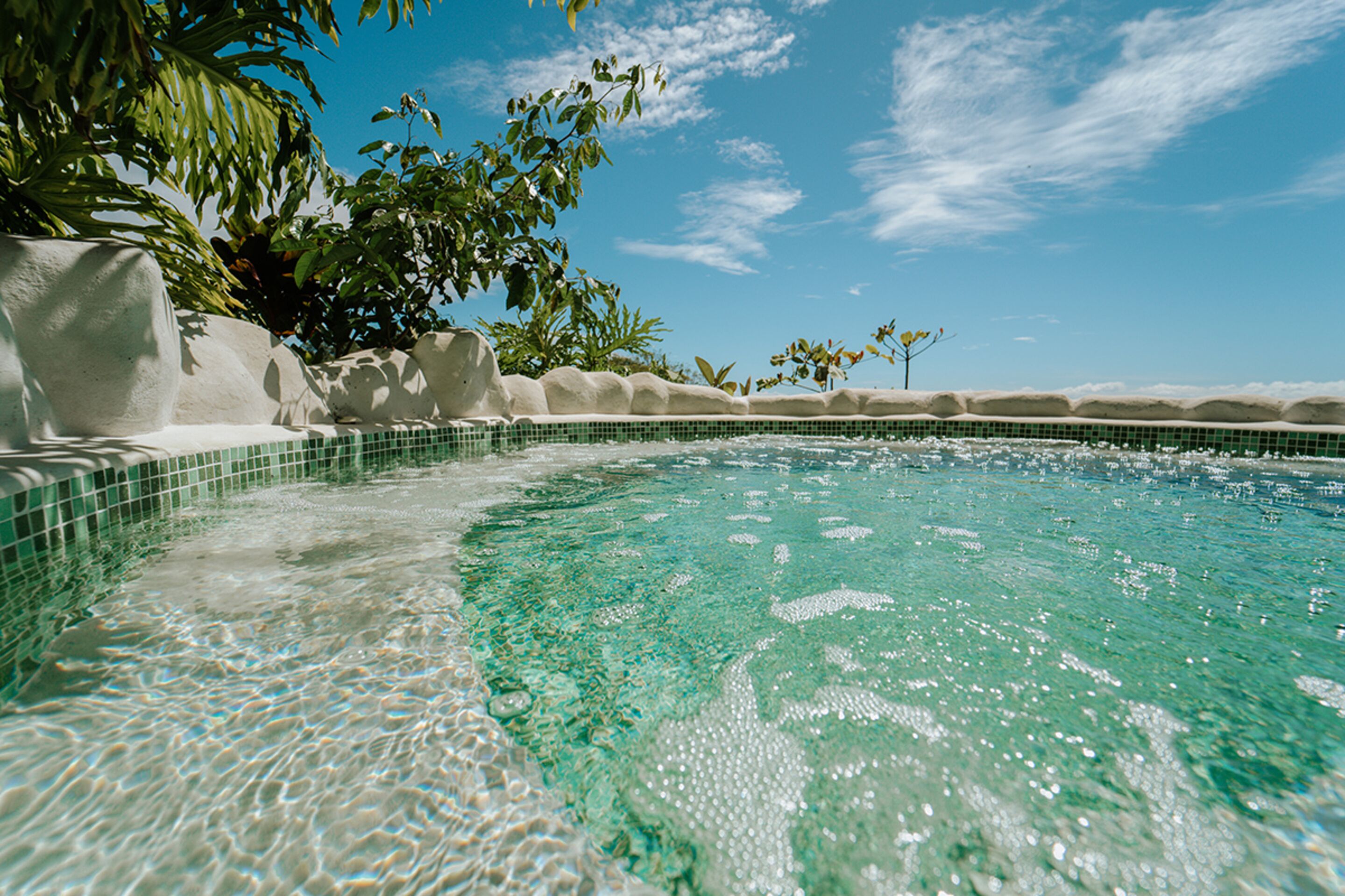 A clear pool with a tiled edge, surrounded by white rock formations and greenery.