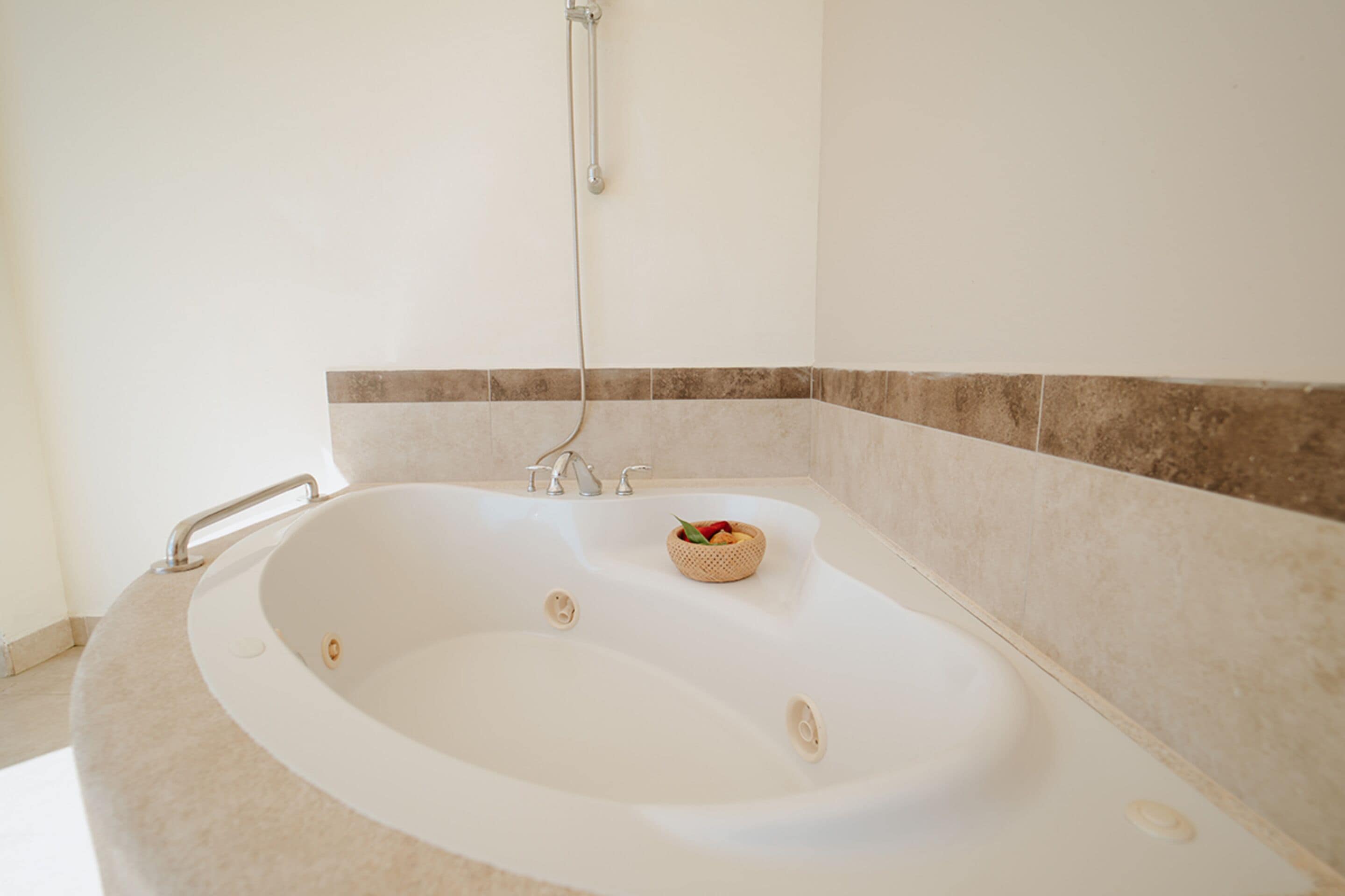 A large bathtub with a handheld showerhead, a small basket with fruits, and a towel rack.
