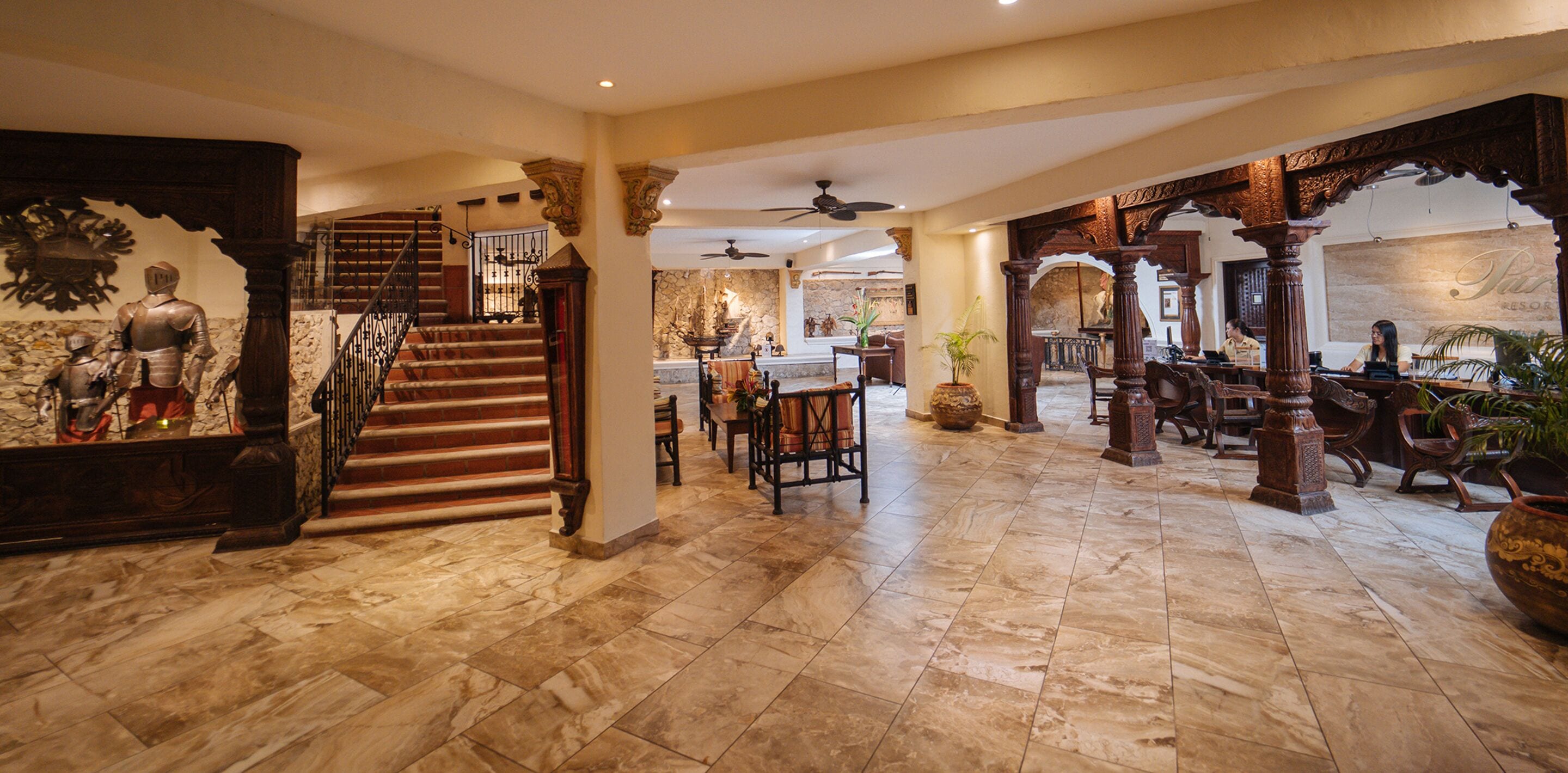 A spacious lobby with a marble floor, a grand staircase, and a seating area with wooden furniture.