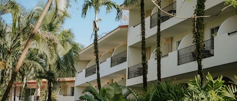 A multi-story hotel with balconies, surrounded by lush tropical vegetation.