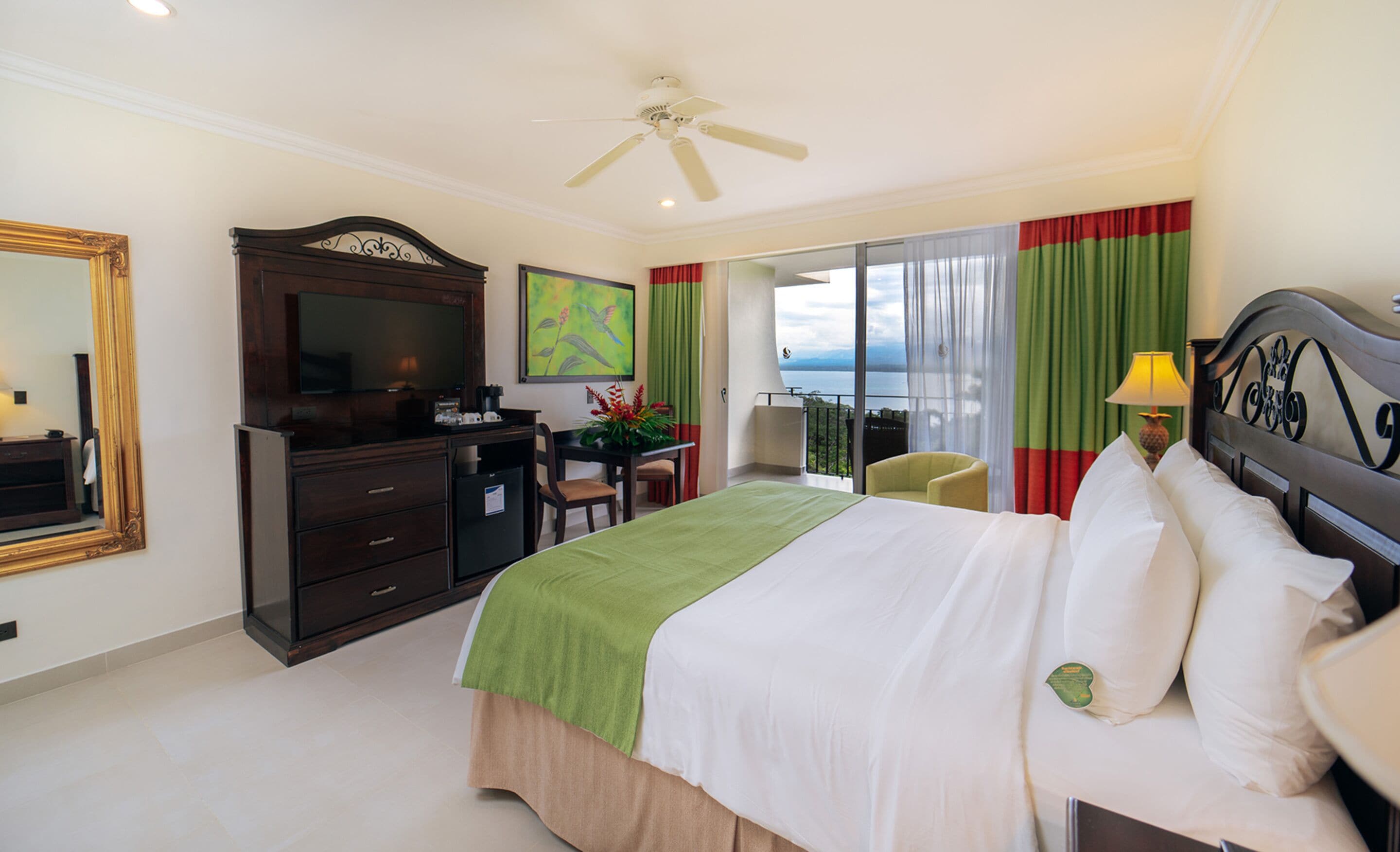 A hotel room with a bed, a desk, a chair, a television, and a balcony with a view.