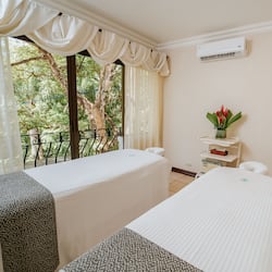Relax on the balcony overlooking lush greenery, featuring two comfortable beds and a charming table setting.