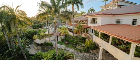 Un resort con piscina, palmeras y un puente que conecta las construcciones.