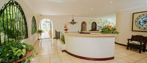A reception area with a curved white counter, a chandelier, and potted plants.