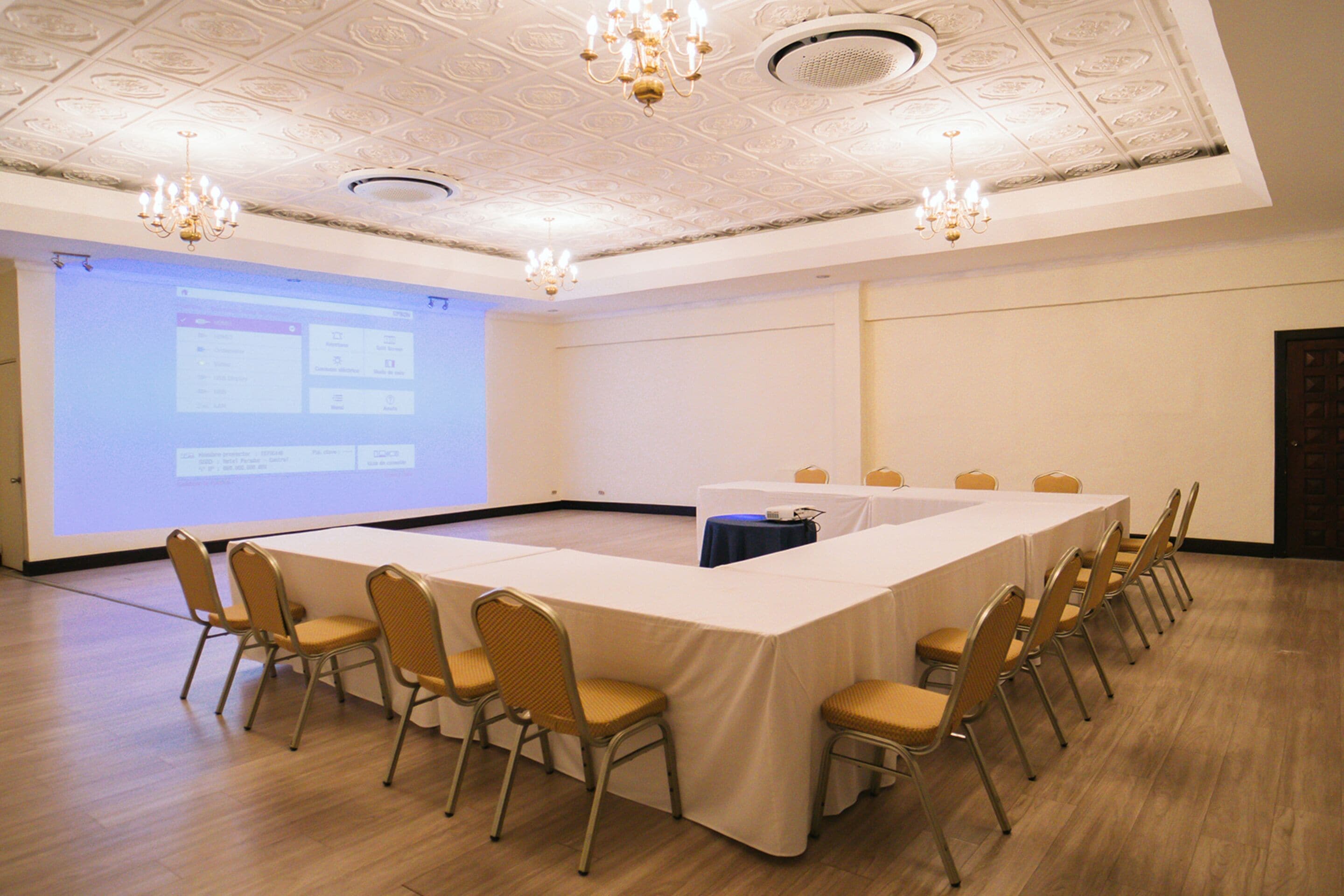 A conference room with a long table, chairs, a projector screen, and chandeliers.