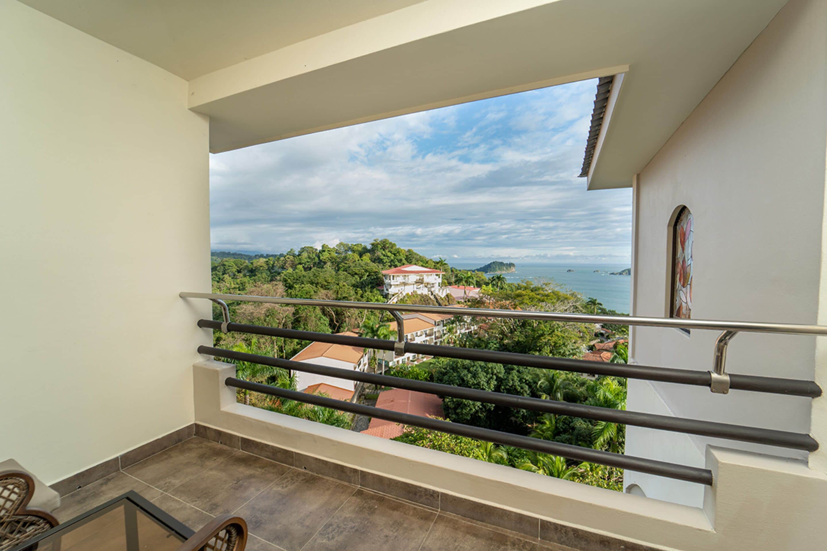 A balcony with a view of a coastal landscape, including a house and the sea.