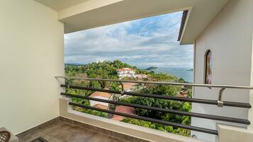A balcony with a view of a coastal landscape, including a house and the sea.