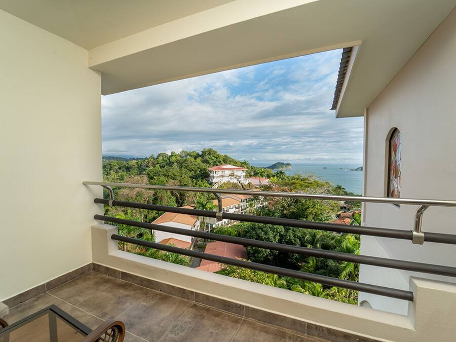 A balcony with a view of a coastal landscape, including a house and the sea.