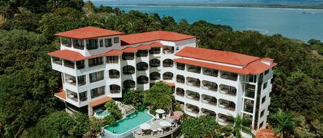 Ein mehrstöckiges Hotel mit Pool, umgeben von üppiger Vegetation und Blick auf das Meer.