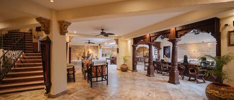 A spacious lobby with a marble floor, a staircase, and a dining area with wooden furniture.