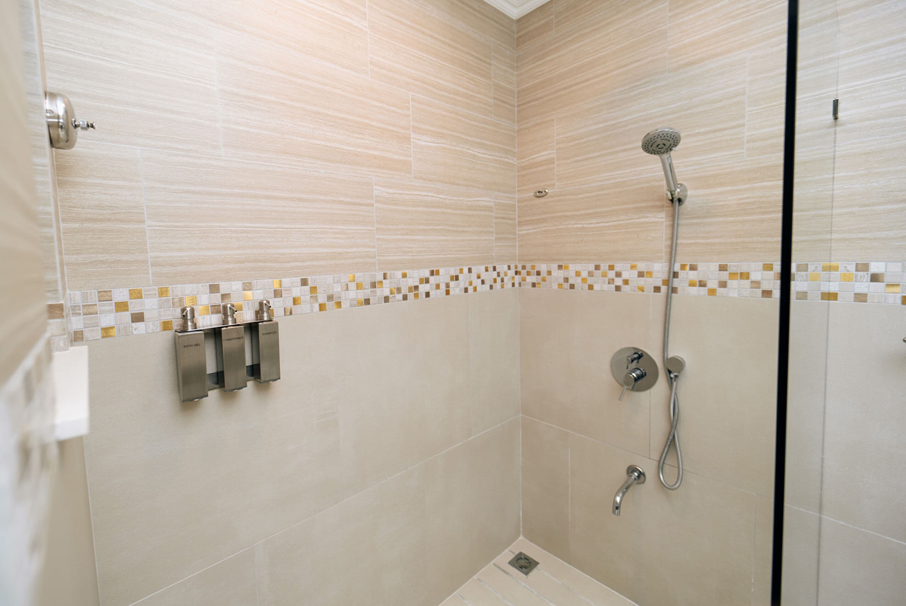 Un baño moderno con cabina de ducha de vidrio, baldosas color beige y un borde de mosaico.