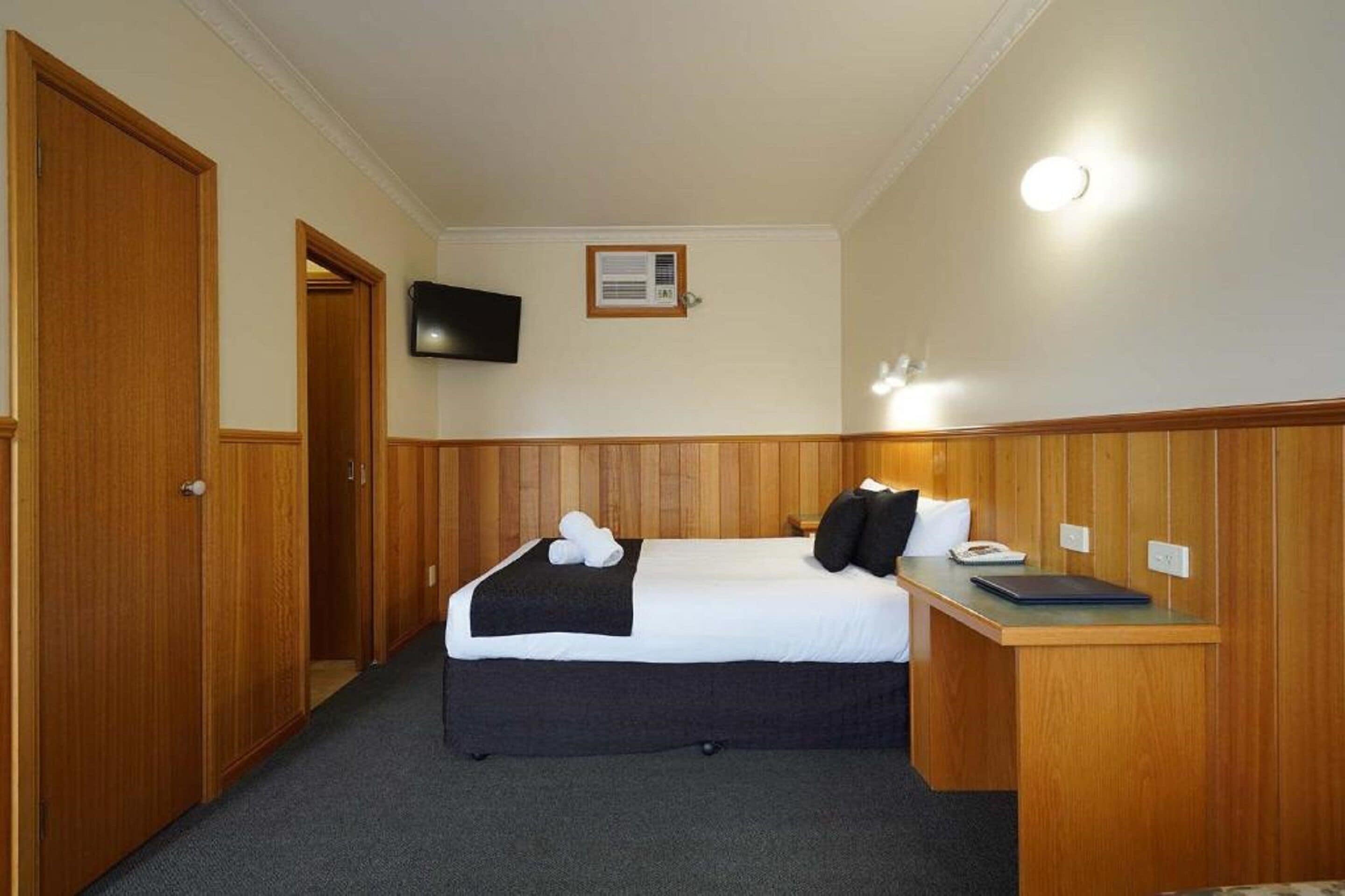 A hotel room with a bed, a desk, a TV, and a door.