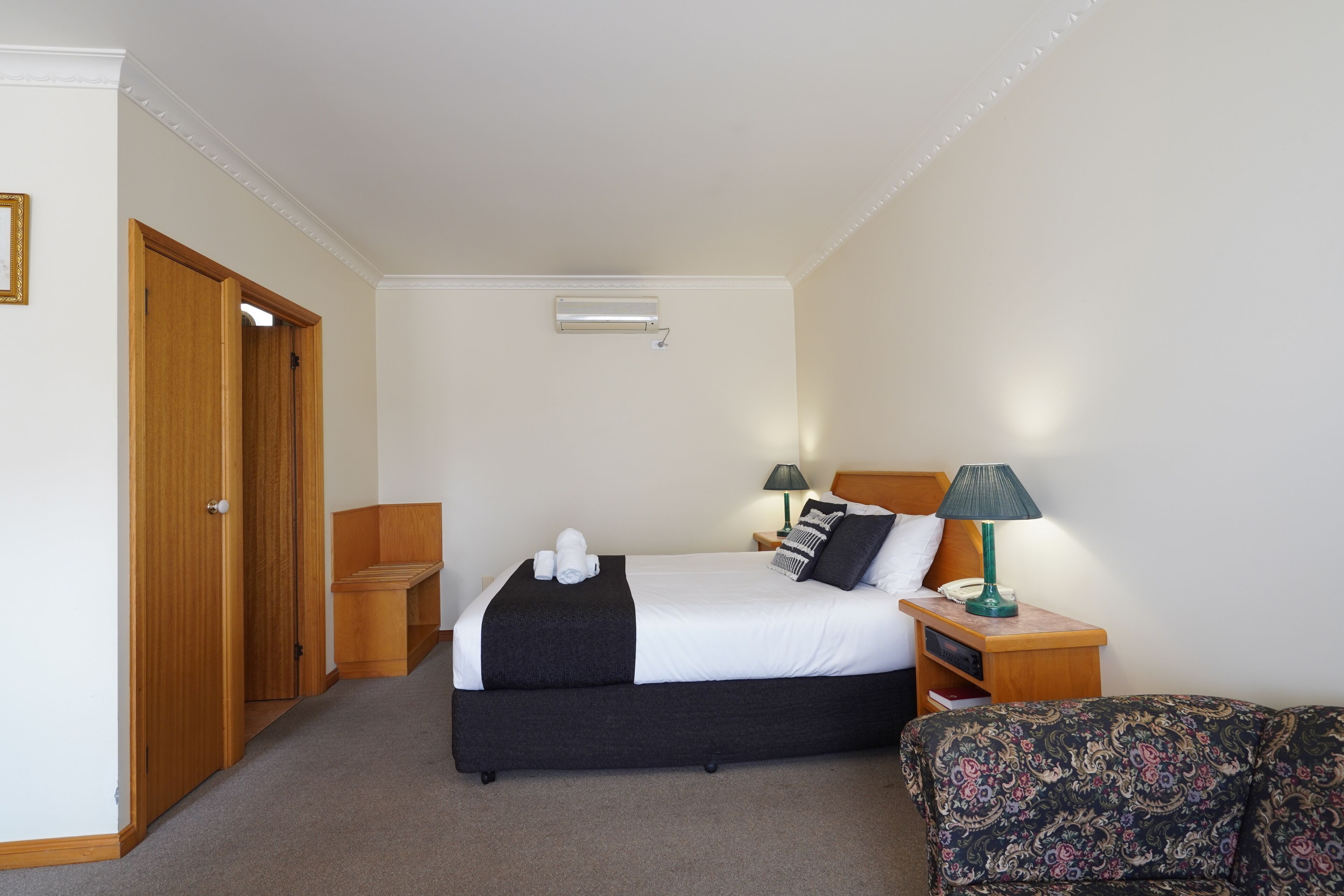 A hotel room with a bed, bedside tables, a lamp, and a patterned sofa.
