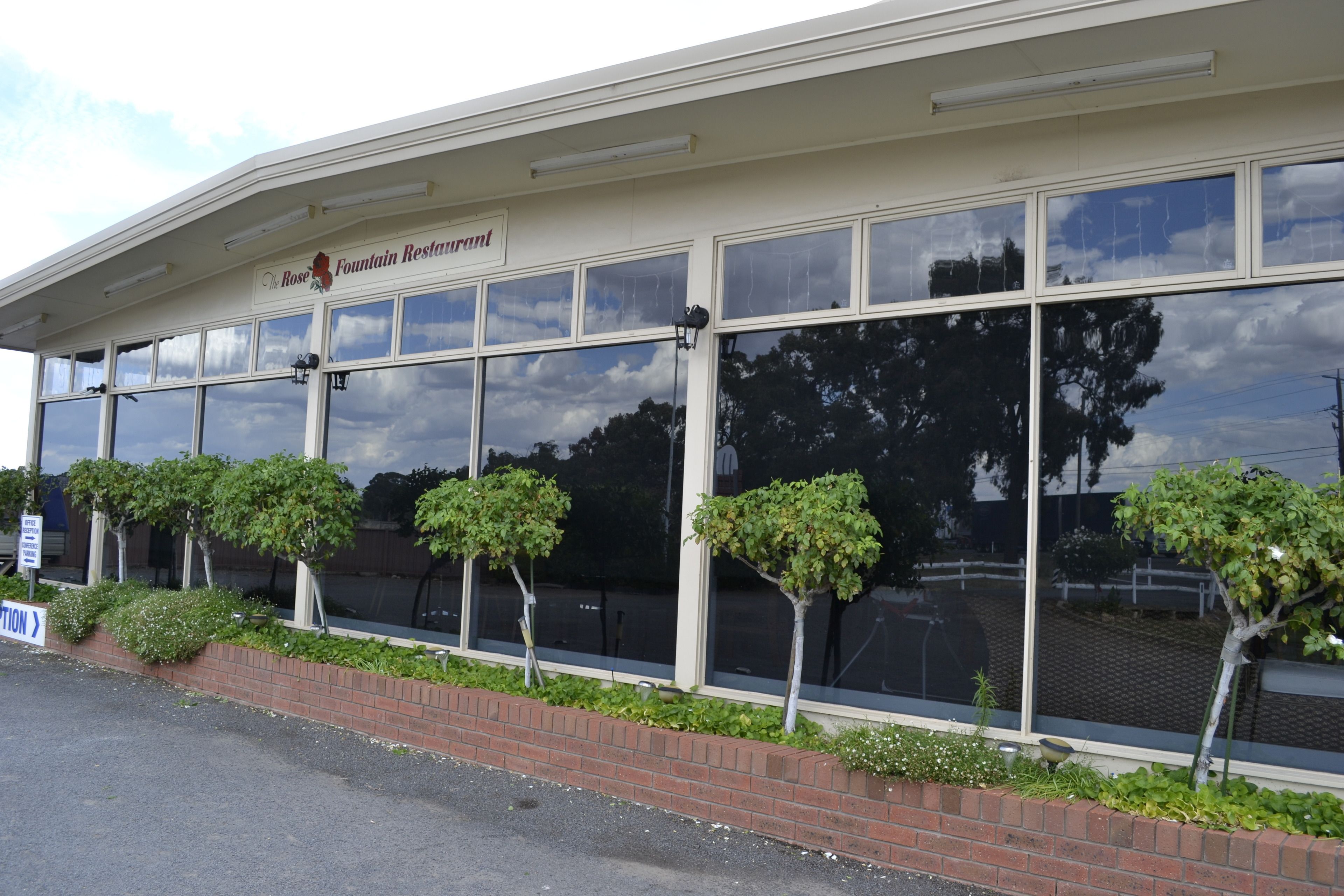 A building with a sign reading "The Rose Fountain Restaurant" and a brick base with small trees.