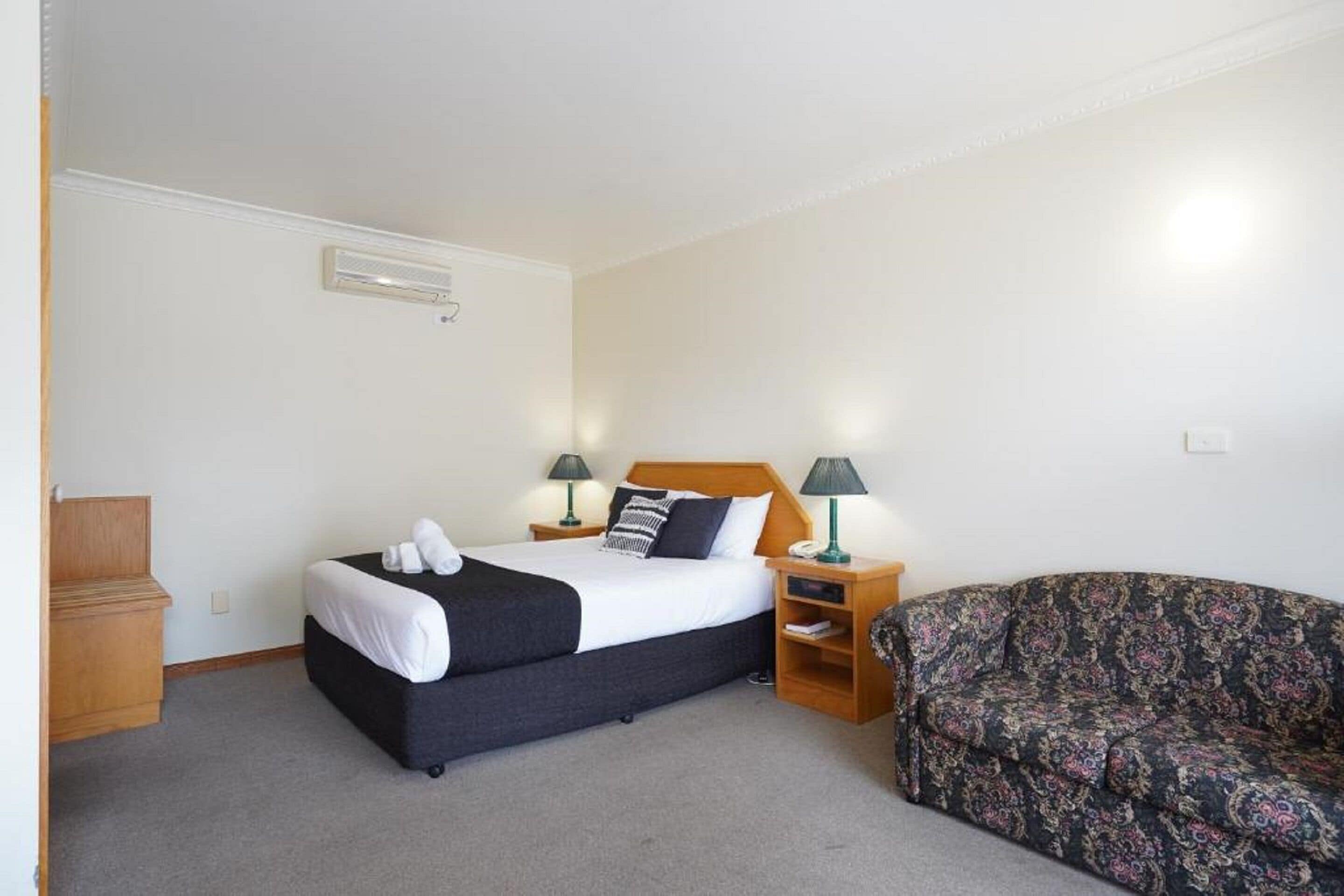 Una habitación de hotel con cama, lámparas de noche, un sofá y una mesita de madera.