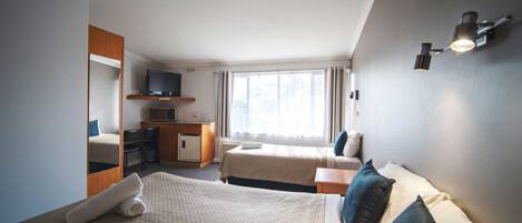 Habitación de hotel con una cama grande, un escritorio, una silla, un televisor y un ventanal con cortinas.