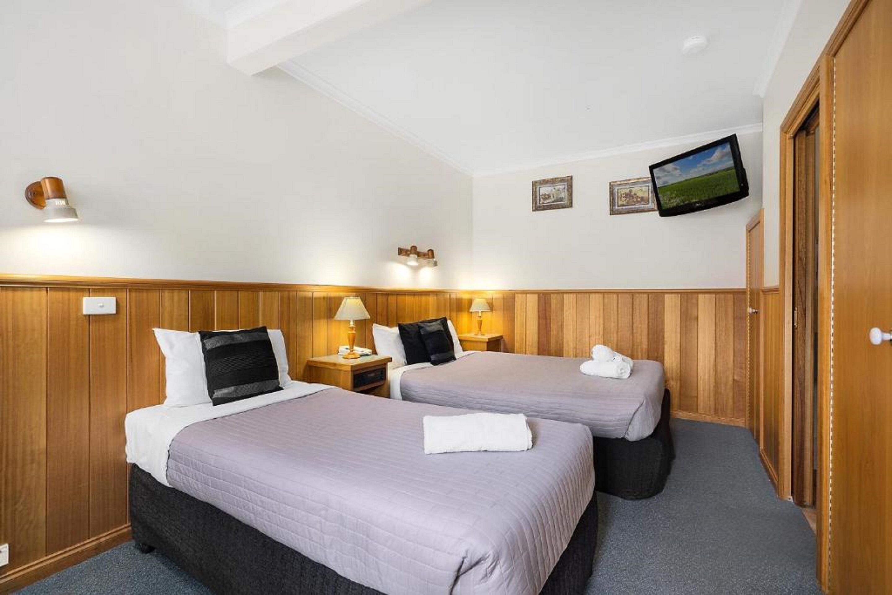 A hotel room with two beds, wooden paneling, a flat-screen TV, and a small painting on the wall.