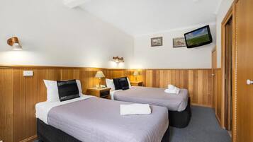 A hotel room with two beds, wooden paneling, a flat-screen TV, and a small painting on the wall.