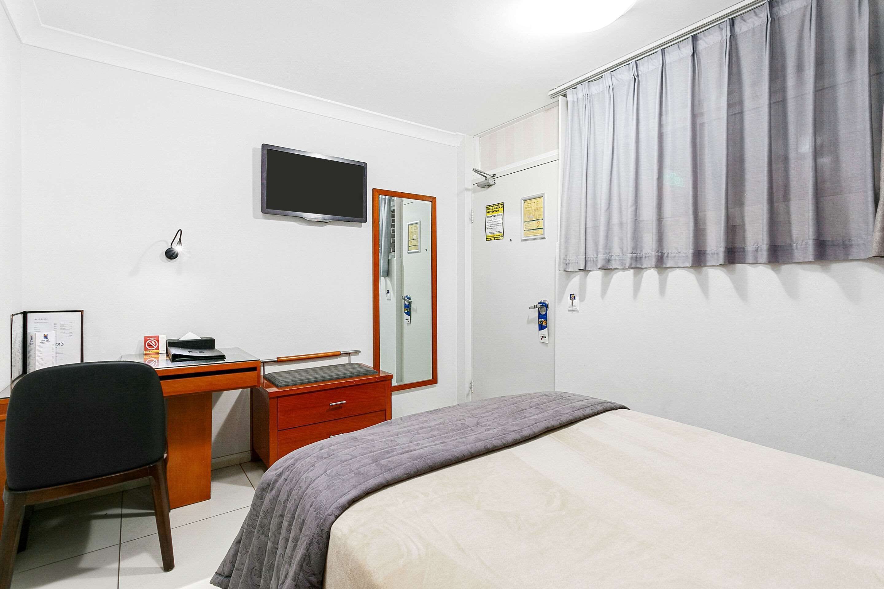 Une chambre à coucher comprenant un lit, un bureau, une chaise, un téléviseur et une porte avec un miroir.