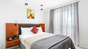 A hotel room with a large bed, a wooden nightstand with a telephone, a painting on the wall, and a window with curtains. - Comfort Inn & Suites Burwood (Burwood)