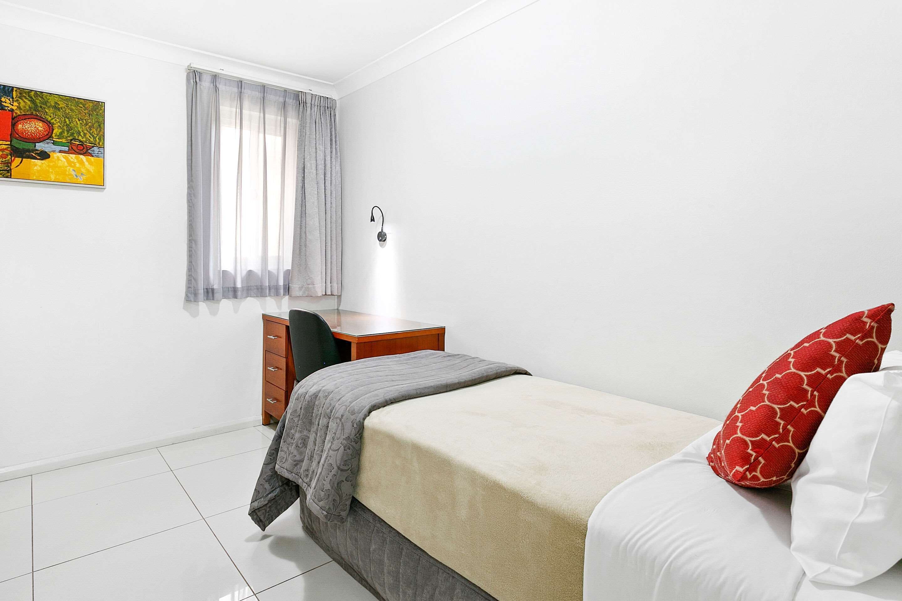 A bedroom with a bed, a desk, a chair, a dresser, and a painting on the wall.