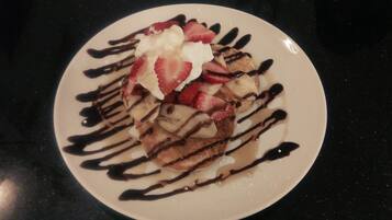A plate of pancakes topped with strawberries, whipped cream, and chocolate syrup.