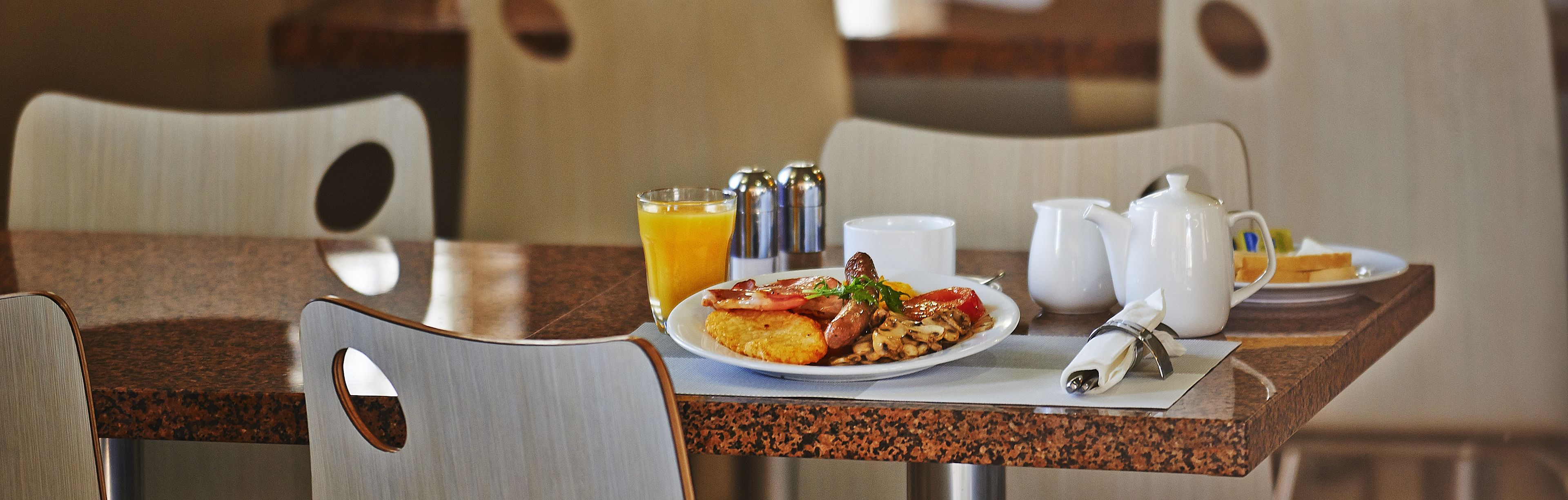 A breakfast table with a plate of food, a glass of orange juice, and a pitcher of water.