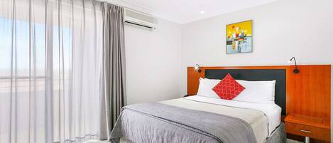 Habitación de hotel con una cama, una mesita de noche, un cuadro en la pared y una ventana con cortinas.