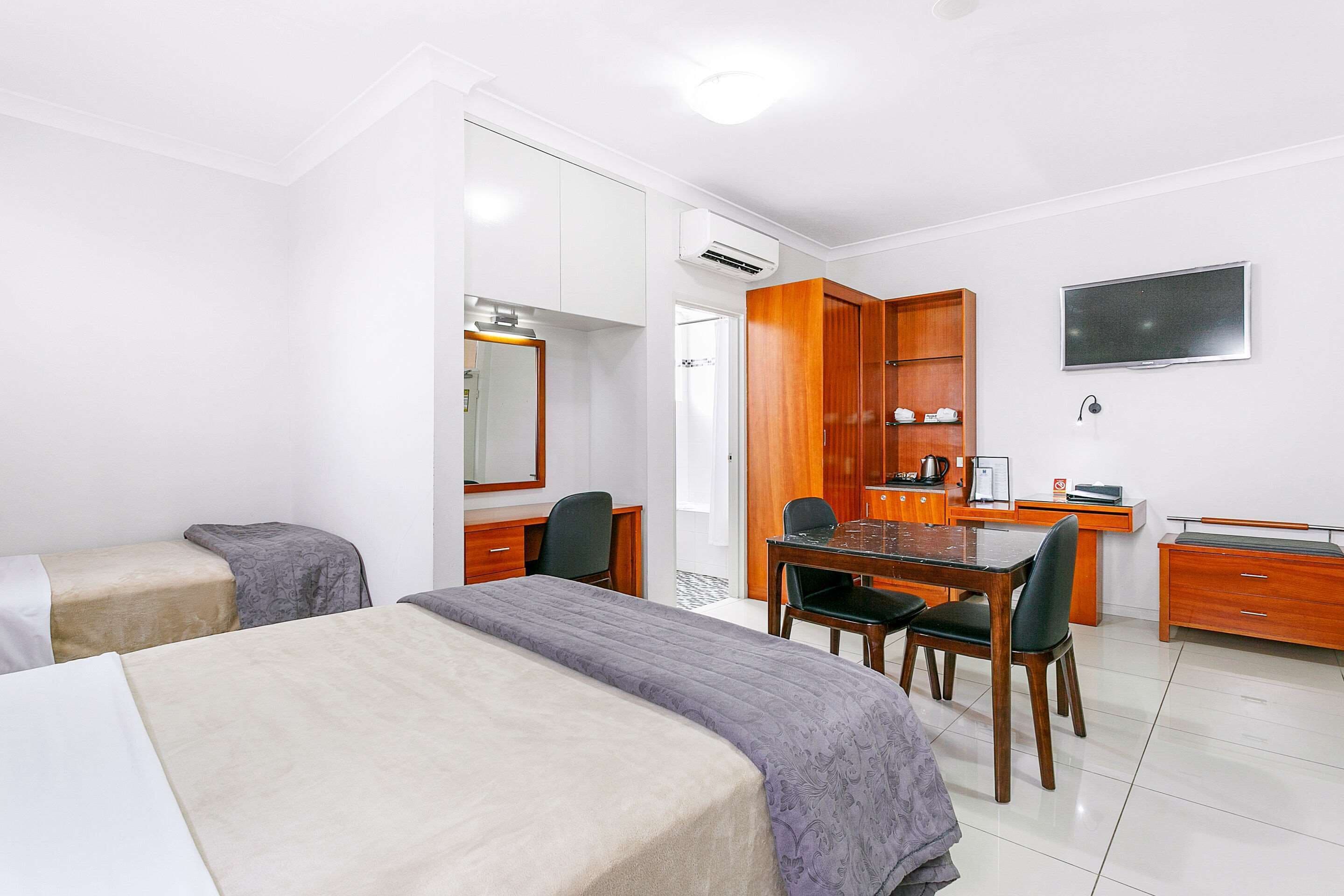 A hotel room with two beds, a desk, a chair, a TV, and a kitchenette.