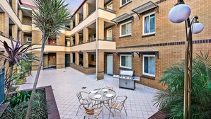 A courtyard with a barbecue grill, outdoor seating, and a palm tree. - Comfort Inn & Suites Burwood (Burwood)