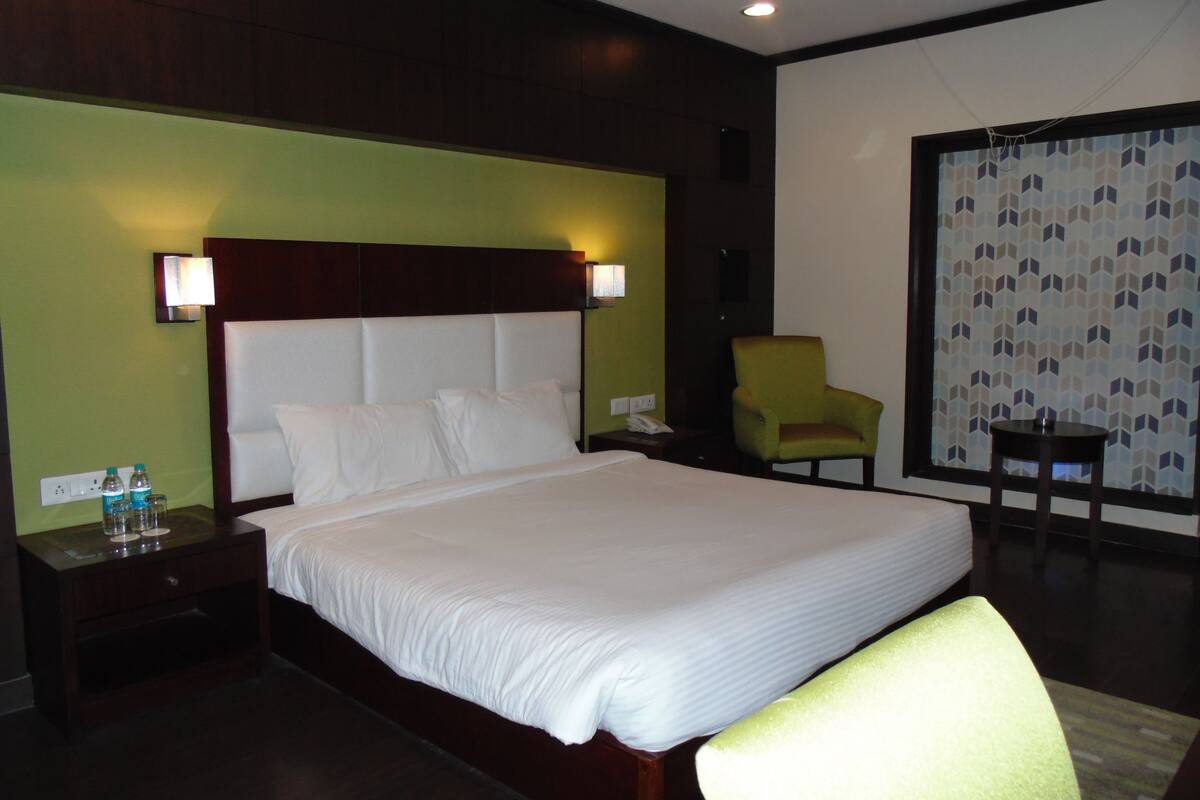A hotel room with a large bed, a nightstand with a lamp, a chair, and a small table.