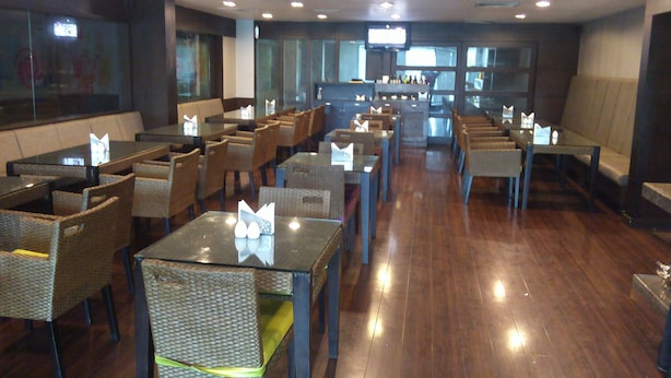 Um restaurante com várias mesas e cadeiras, uma área de bar e uma tela de televisão.