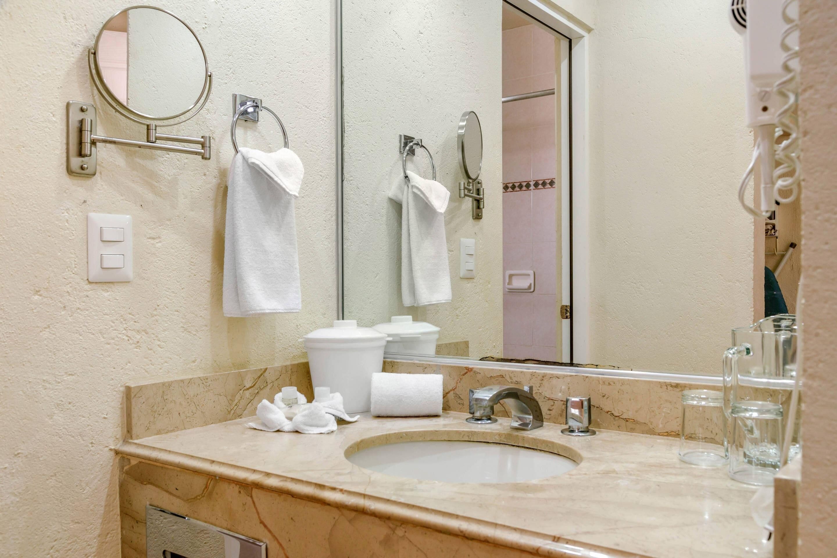 A bathroom with a sink, mirror, towel rack, and a toilet paper holder.