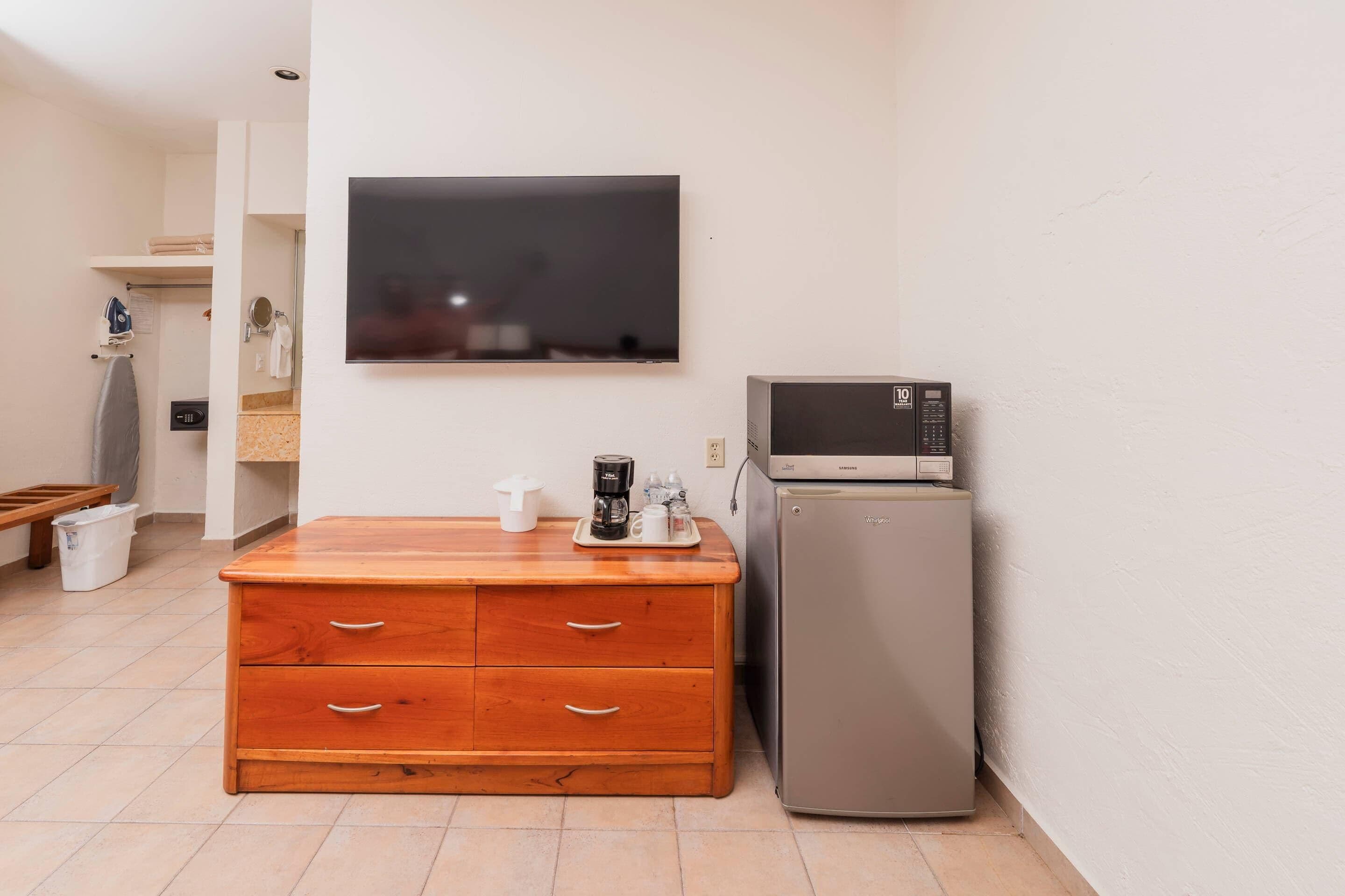 A room with a wooden dresser, a flat-screen TV, a microwave, and a refrigerator.