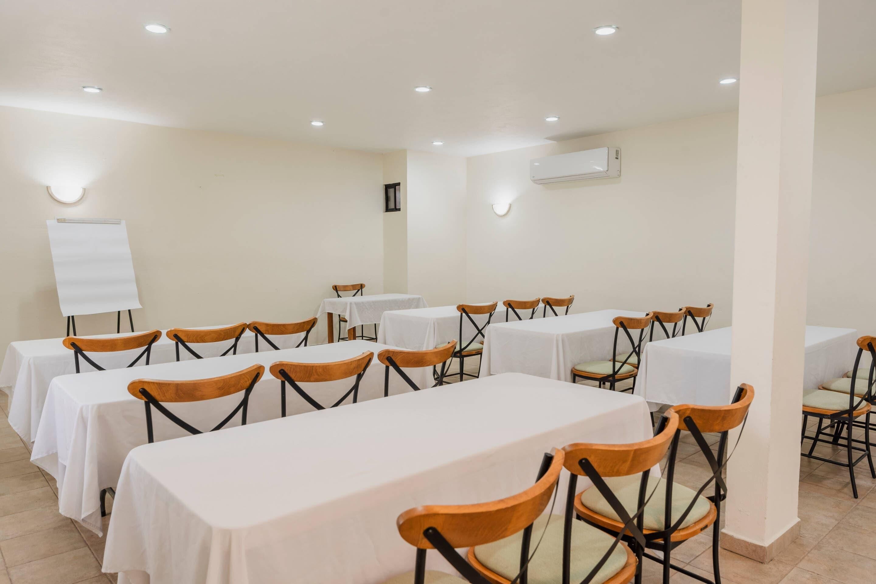 A conference room with tables and chairs, white walls, and recessed ceiling lights.
