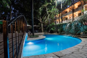 Una piscina con una cascada de piedra, rodeada de palmeras y un muro de piedra.