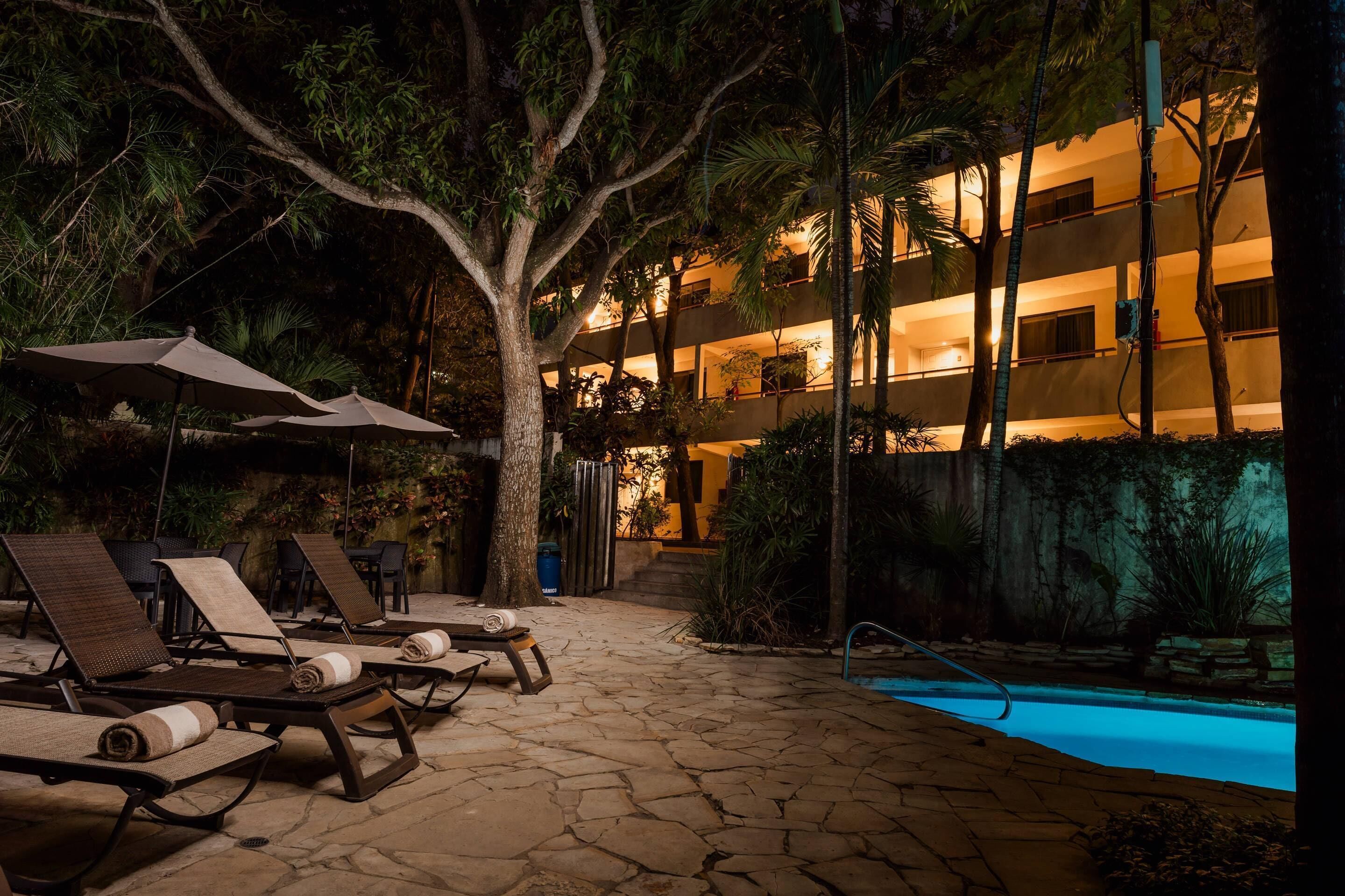 A poolside area with lounge chairs and umbrellas, a stone pathway, and a building with multiple balconies.